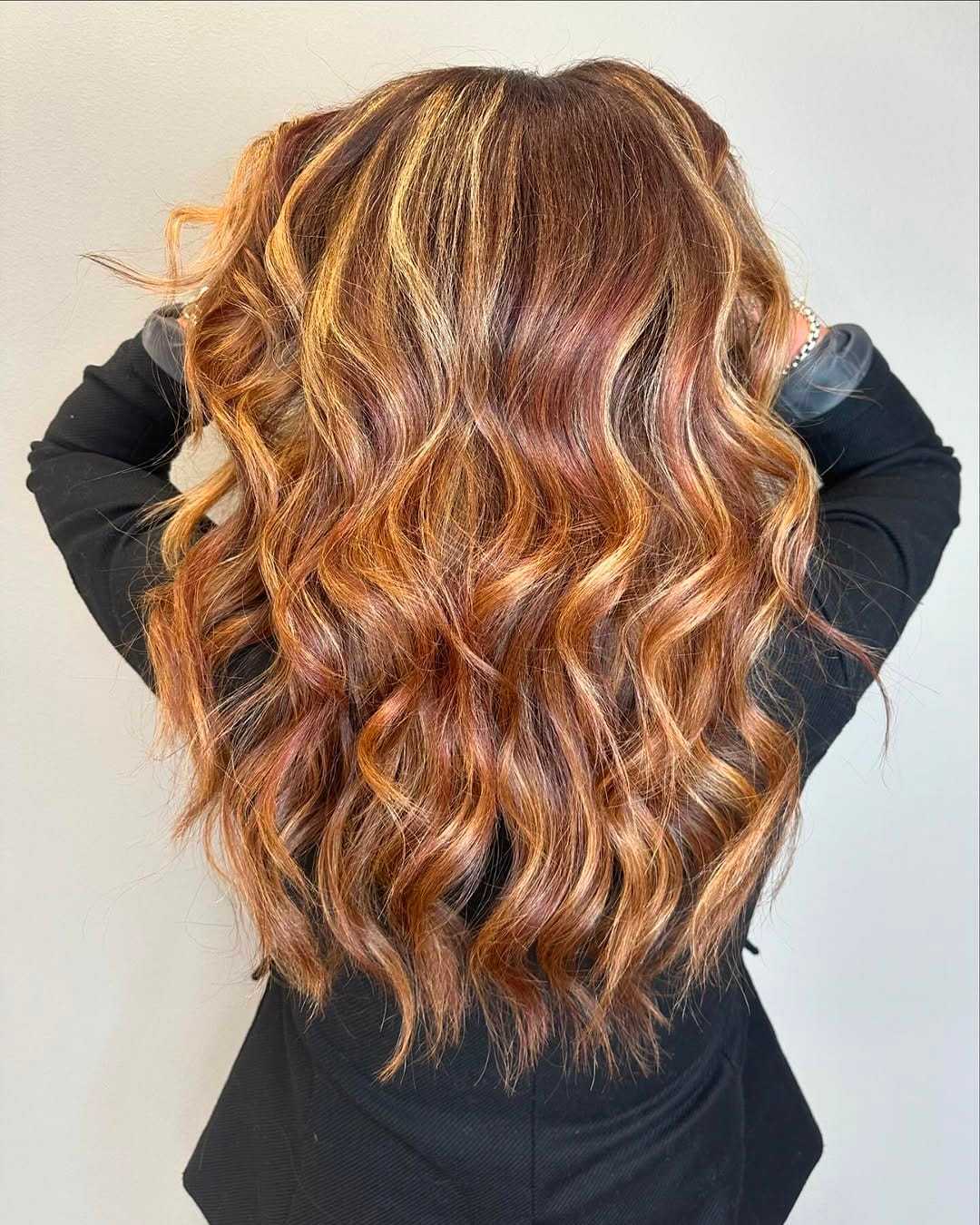 Wavy, highlighted hair cascading down the back of a person in a black outfit.