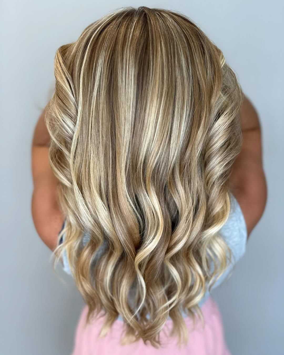 Wavy blonde hair with highlights displayed from the back against a neutral background.