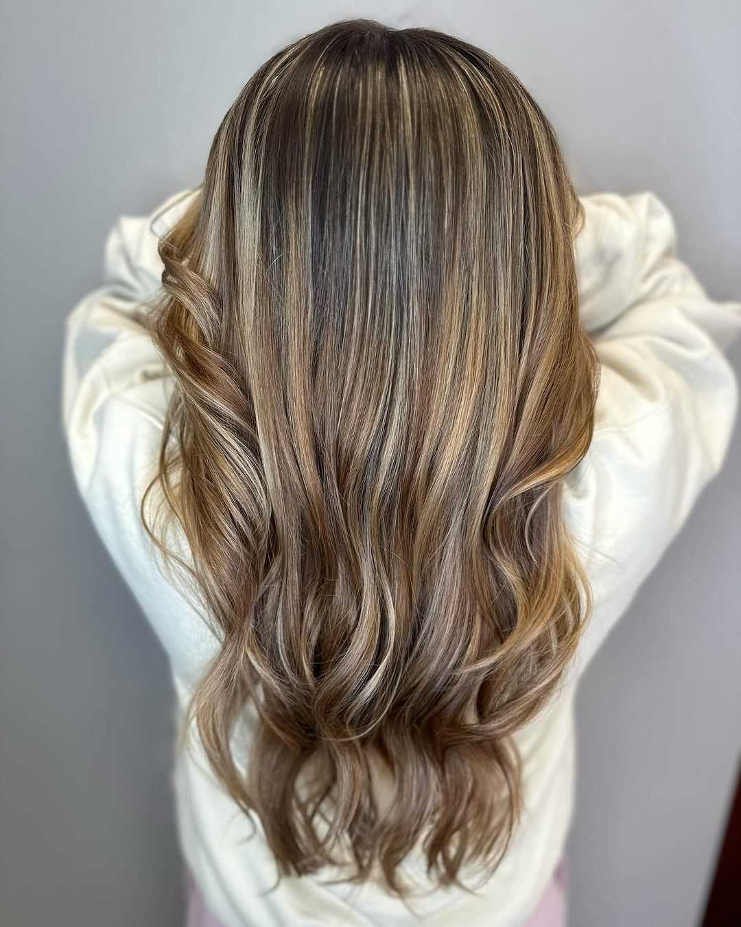 Long, wavy brown hair with blonde highlights, shown from the back against a neutral background.